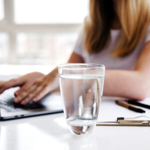 Frau arbeitet am Computer und ein Wasserglas steht neben ihr.