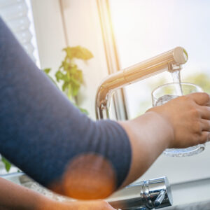 Person hält Wasserglas unter fließenden Wasserhahn.